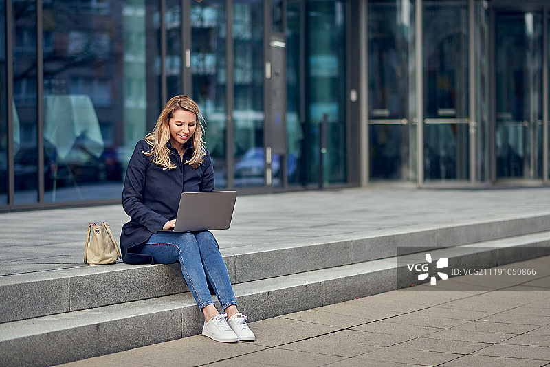 在小镇使用笔记本电脑的迷人金发女子图片素材
