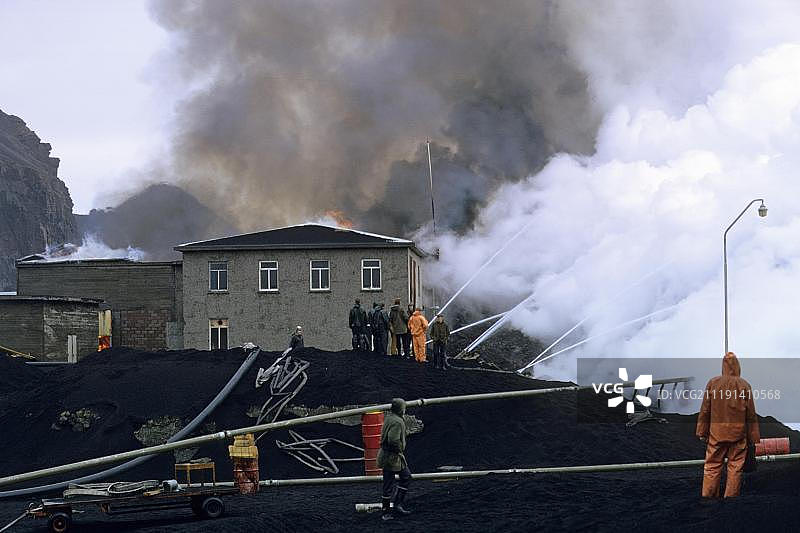 火山爆发，建筑物被熔岩和火山灰吞没，用水减缓熔岩流动，埃尔德费尔火山，赫马岛，韦斯特曼群岛，冰岛，1973年图片素材