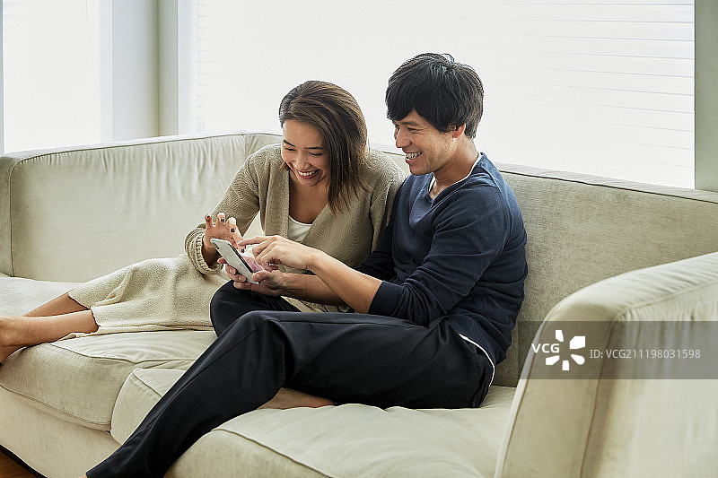 微笑的中年夫妇在沙发上使用智能手机图片素材