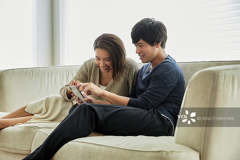 微笑的中年夫妇在沙发上使用智能手机图片素材