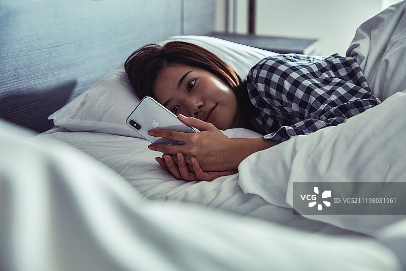年轻女人在床上使用智能手机图片素材