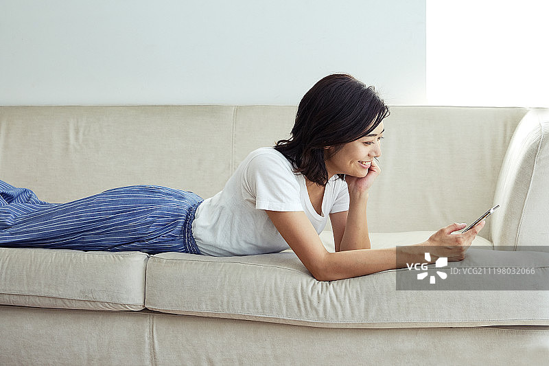 躺在沙发上使用智能手机的年轻女人图片素材