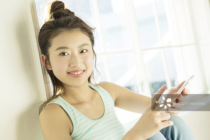 微笑的年轻女人在窗边使用智能手机图片素材