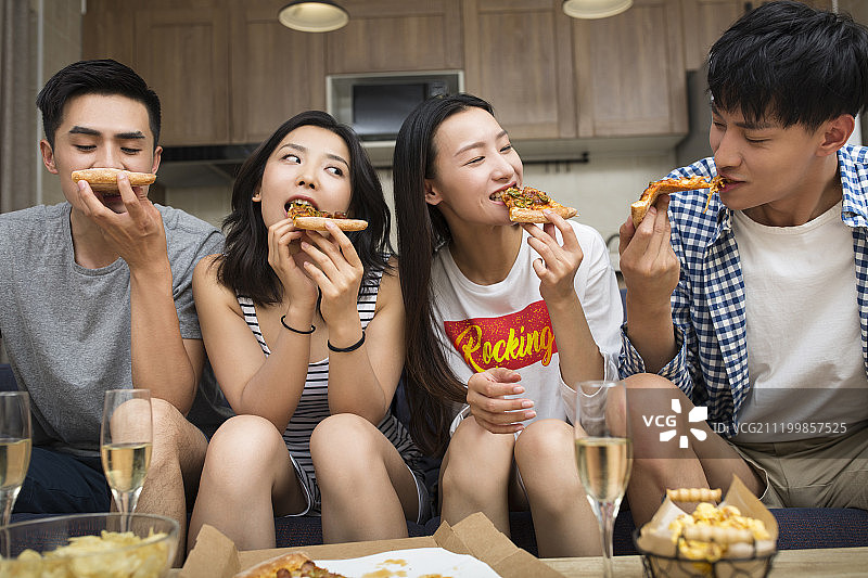 快乐的年轻人在客厅吃披萨图片素材