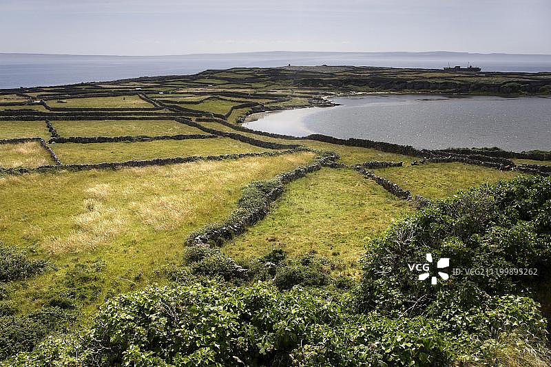 岩石和石墙，农田景观与远处的普拉西沉船，爱尔兰共和国伊尼希尔岛，欧洲图片素材