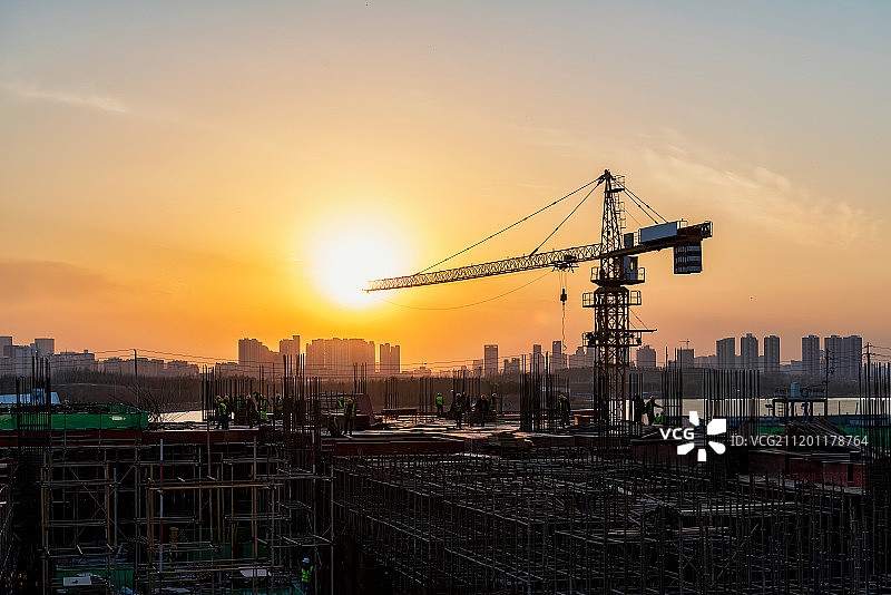 起落时分建筑工地塔吊与城市天际线逆光剪影图片素材