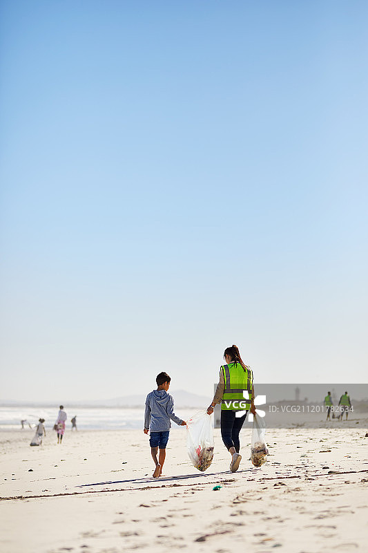 阳光明媚的沙滩上，母子志愿者清理垃圾图片素材