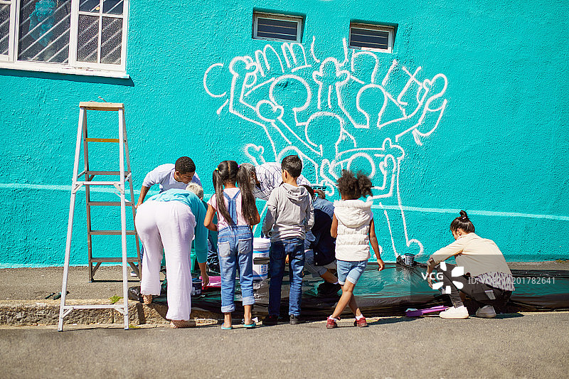 孩子们在阳光明媚的墙上绘制社区壁画图片素材