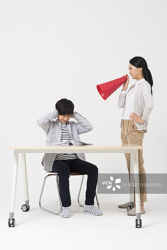 青少年男孩坐在书桌前，女人站在旁边训斥的摄影图片素材
