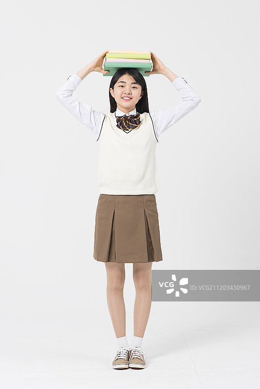 身穿校服头顶书本的少女摄影图片素材