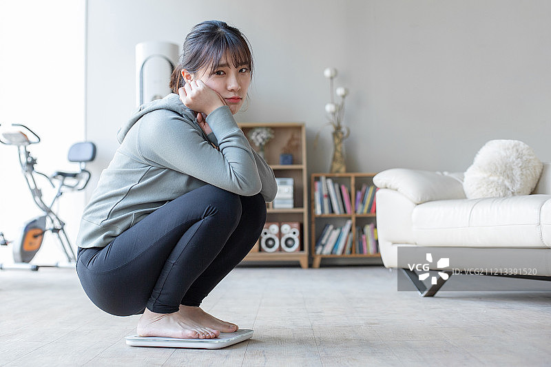 女人在客厅，体重秤显示令人失望的节食结果，坐在地上抱怨图片素材