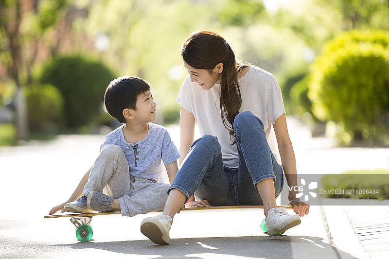 年轻妈妈和儿子坐在滑板上图片素材