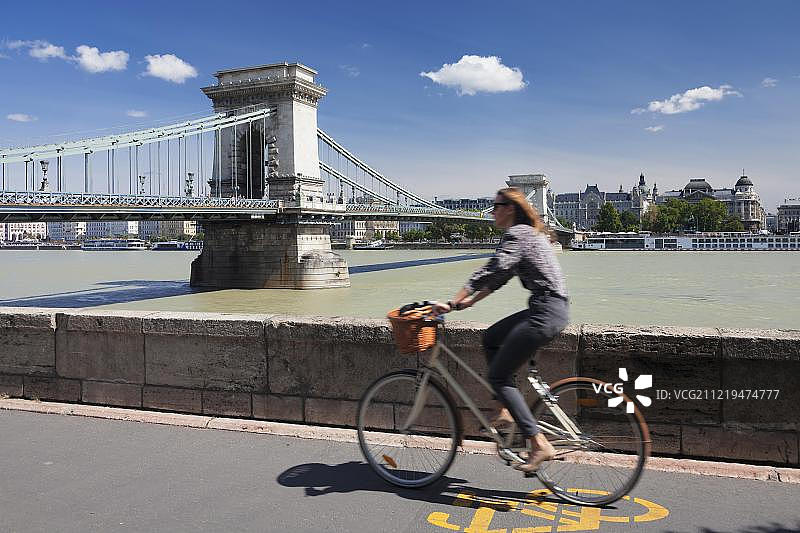 骑自行车的人在多瑙河畔，远处是匈牙利布达佩斯的塞切尼链桥图片素材