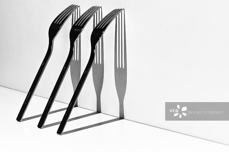倚靠在白墙上并投下阴影的餐叉图片素材