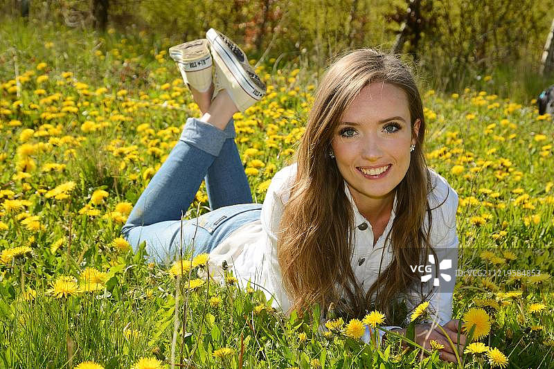 年轻女人躺在蒲公英草地上，于斯塔德，斯科纳，瑞典，欧洲图片素材