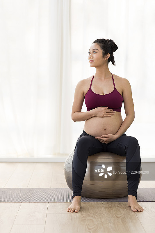 年轻孕妇坐在瑜伽球上图片素材