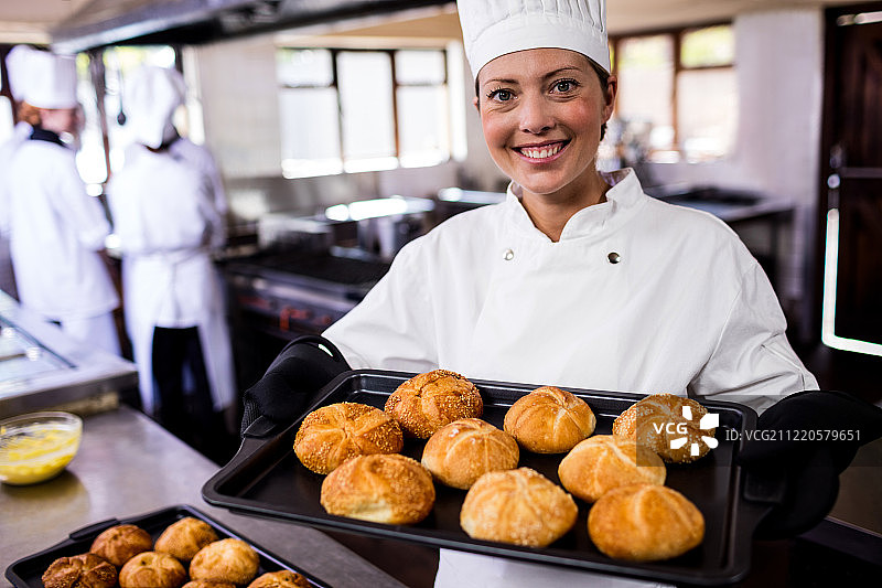 女厨师们在酒店厨房里拿着一盘烤好的面包卷图片素材
