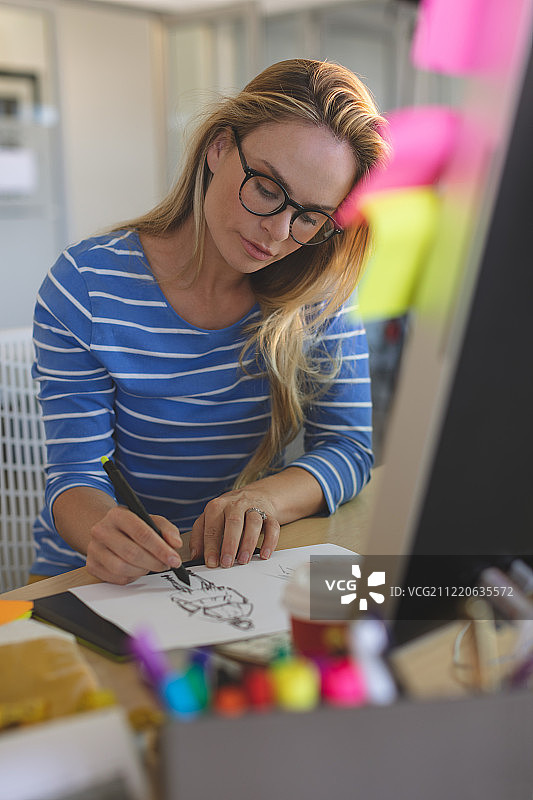年轻白人女性时装设计师在现代办公室的桌子上画草图的正面照图片素材