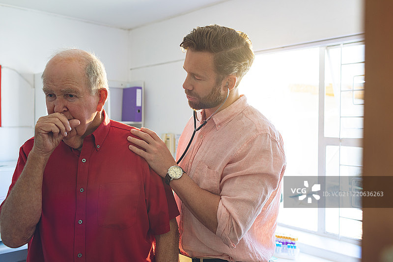 一位年长的白人医生用听诊器检查一位正在咳嗽的老年病人正面照图片素材