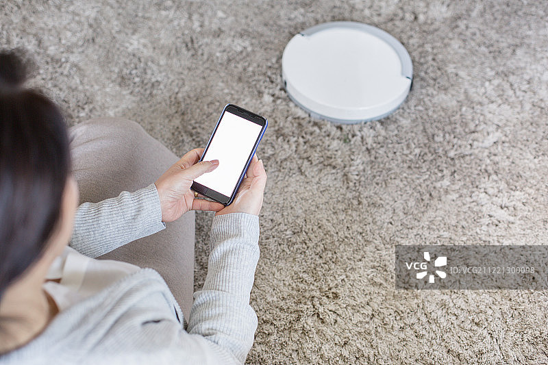 客厅，中年妇女，全职太太，扫地机器人，无线技术，智能手机，蓝牙图片素材