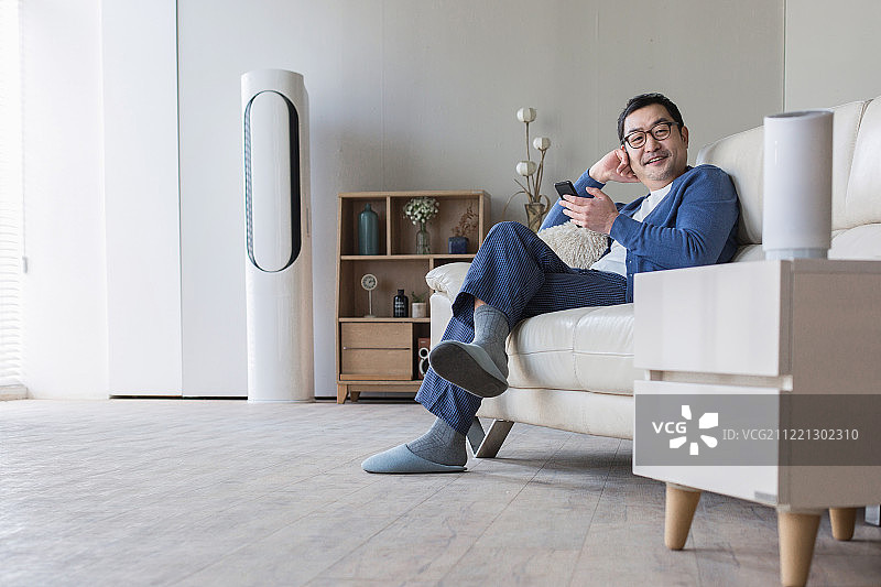 中年男性在客厅使用AI智能音箱和蓝牙智能手机，面带微笑图片素材