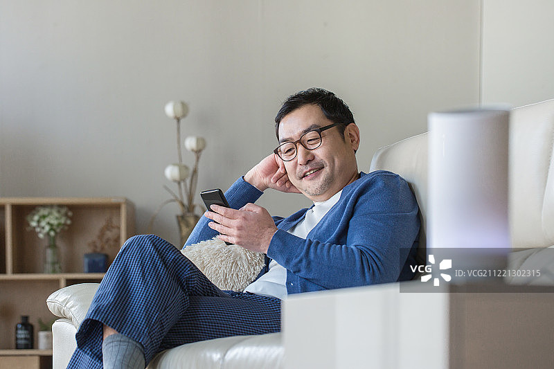 中年男性在客厅使用AI智能音箱和蓝牙智能手机，面带微笑图片素材