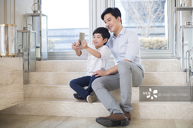 快乐的父子在客厅使用手机自拍图片素材