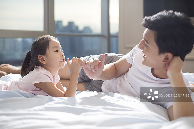 快乐年轻父女在床上拉勾图片素材