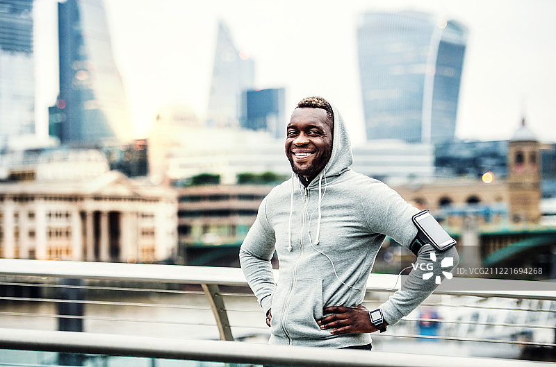 在城市桥上休息的戴智能手表和智能手机的黑人跑步者图片素材