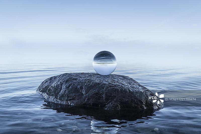 蓝色海洋边黑色岩石上的水晶球图片素材