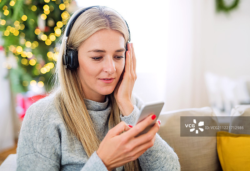 圣诞节在家戴耳机用智能手机的年轻女子图片素材