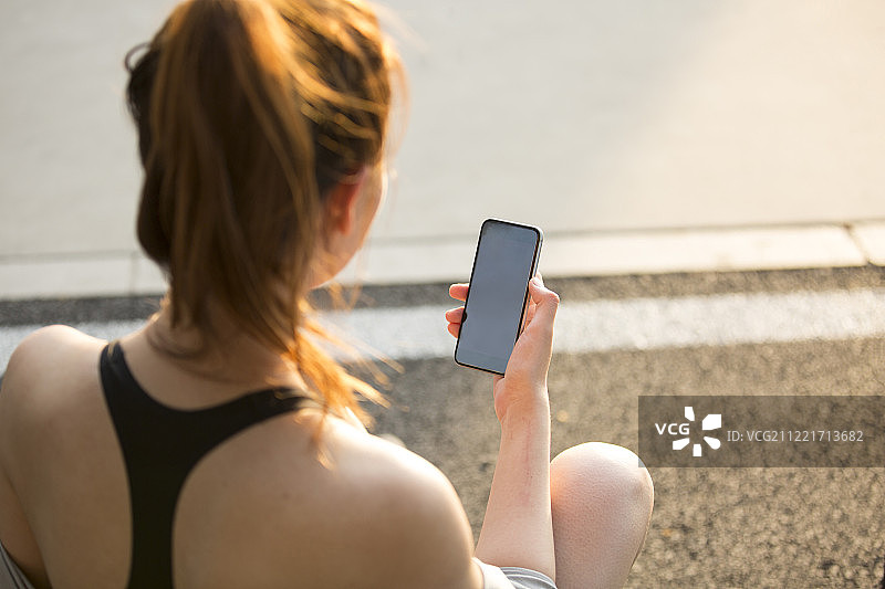 青年女子在户外运动后坐在地上玩手机休息图片素材