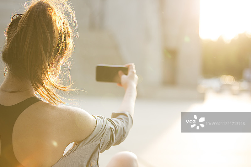 青年女子在户外运动后坐在地上玩手机休息图片素材