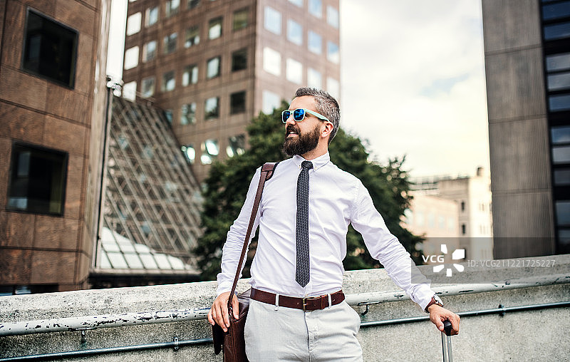 戴太阳镜和笔记本电脑包的时尚商人在伦敦的街道上图片素材