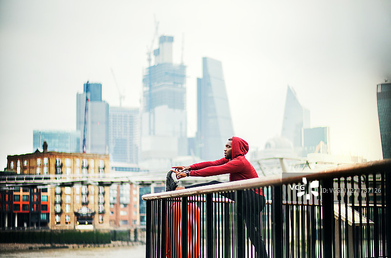年轻的黑人运动型男子在城市大桥外伸展腿部图片素材