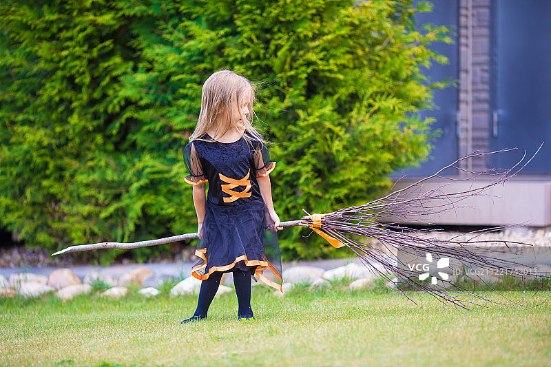 万圣节穿着女巫服装的可爱小女孩在秋日进行不给糖就捣蛋活动图片素材