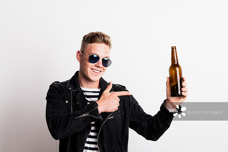 在工作室里戴着太阳镜，拿着空啤酒瓶的自信的年轻人图片素材