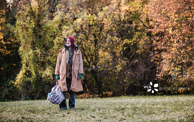 流浪乞丐在公园户外站立，拿着包，留白图片素材