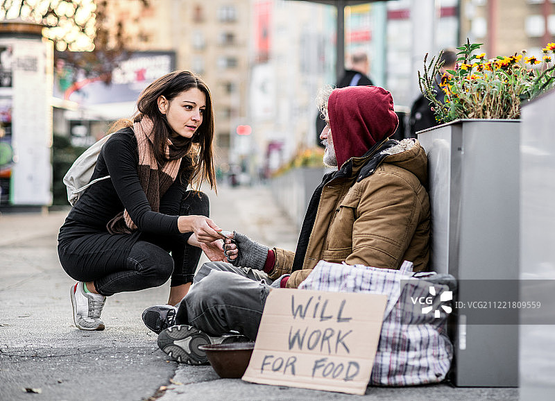 年轻女人在城市给流浪汉钱图片素材
