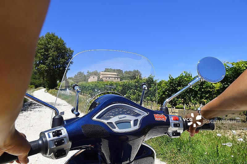 女人骑着Vespa Primavera摩托车行驶在意大利马尔凯莫罗达尔巴的圣阿米科葡萄酒产区图片素材