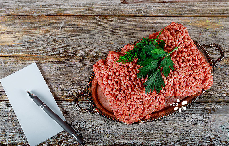 生牛肉馅、香草、笔记本和笔，置于旧木背景上图片素材