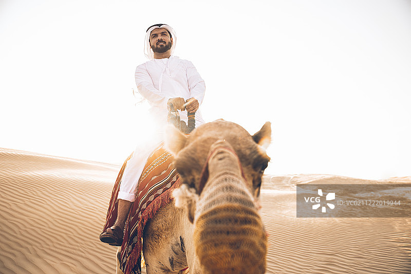 穿着传统服装，牵着骆驼在沙漠中行走的男人图片素材
