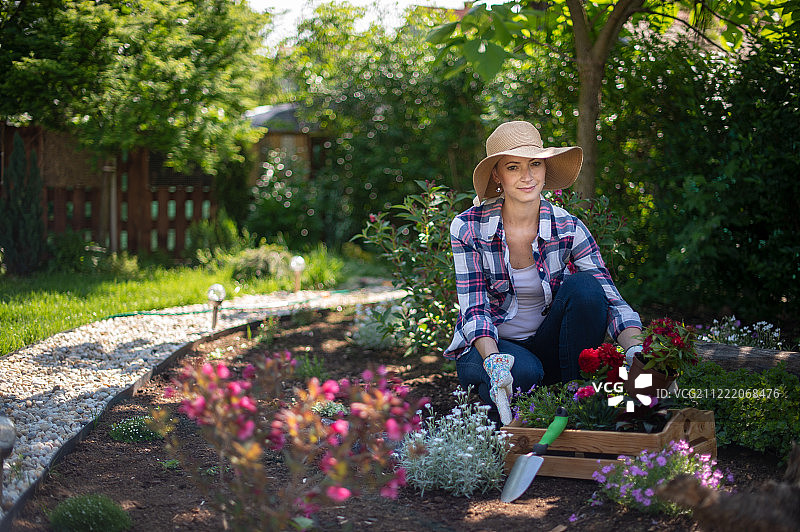 看着镜头微笑并抱着装满鲜花的木箱的美丽女园丁图片素材