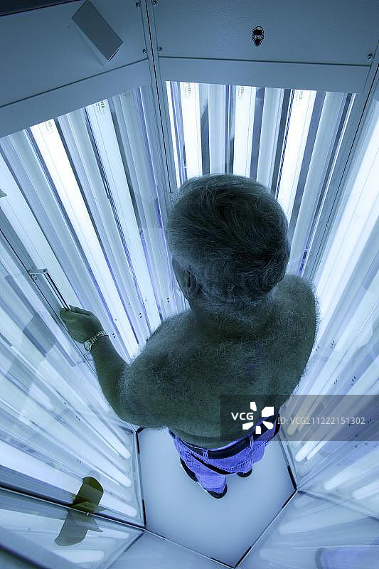 在德国，男子站在皮肤科诊所的紫外线光疗舱内接受紫外线光疗图片素材