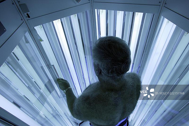 在德国，男子站在皮肤科诊所的紫外线光疗舱内接受紫外线光疗图片素材