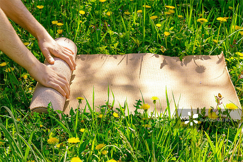 夏季晴朗的一天，男子在绿色草地上瑜伽课后收起垫子图片素材