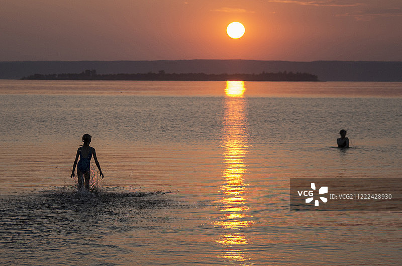 儿童在日落时于河中游泳图片素材