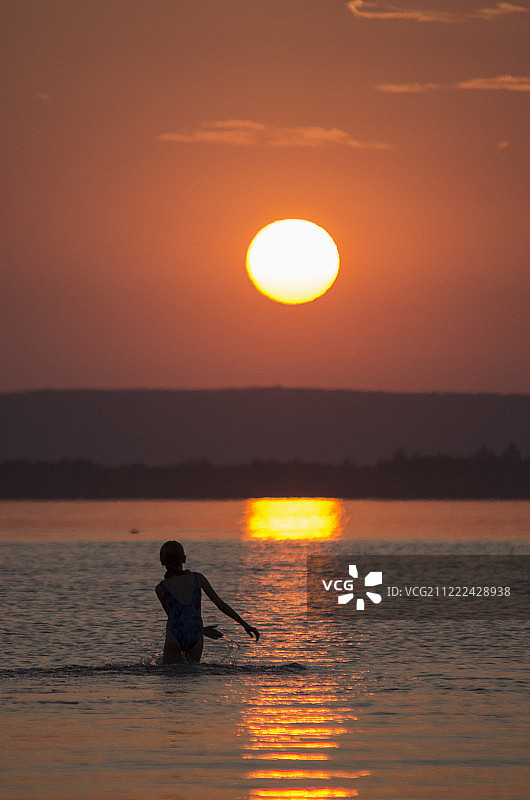 儿童在日落时于河中游泳图片素材