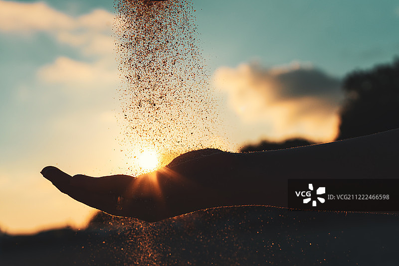 在海滩上倾倒沙子的年轻女孩的手的剪影图片素材