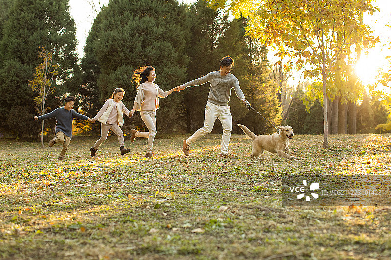 快乐的年轻家庭和狗在秋日的树林里图片素材